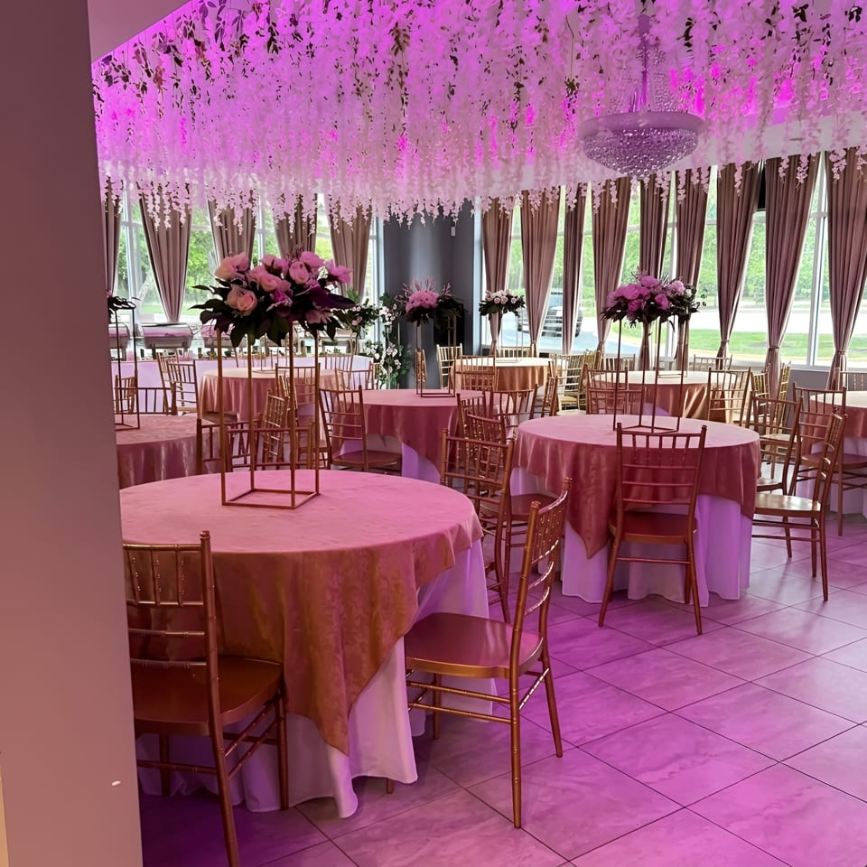 Elegant dining room with pink tablecloths, gold chairs, floral centerpieces, and hanging white wisteria.