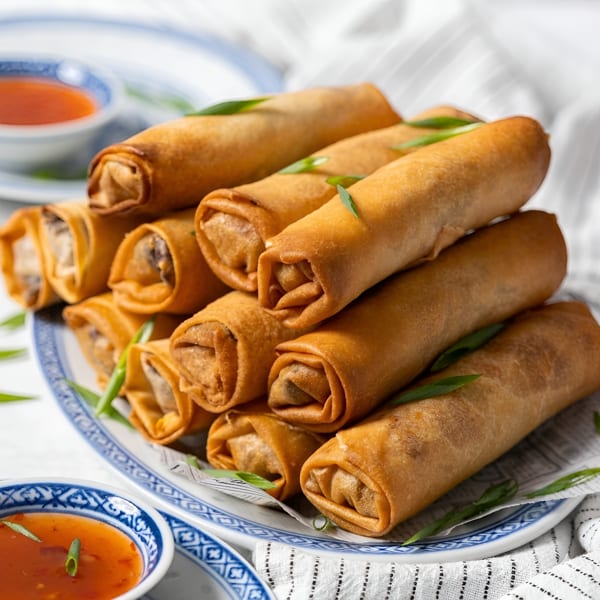A stack of crispy golden spring rolls garnished with green onions on a white and blue plate.
