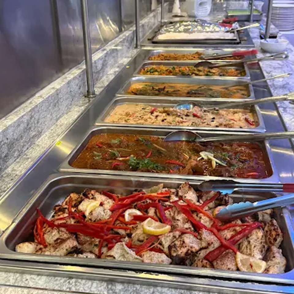 Buffet counter displaying trays of grilled chicken, red peppers, vegetables, rice, and sauced dishes.