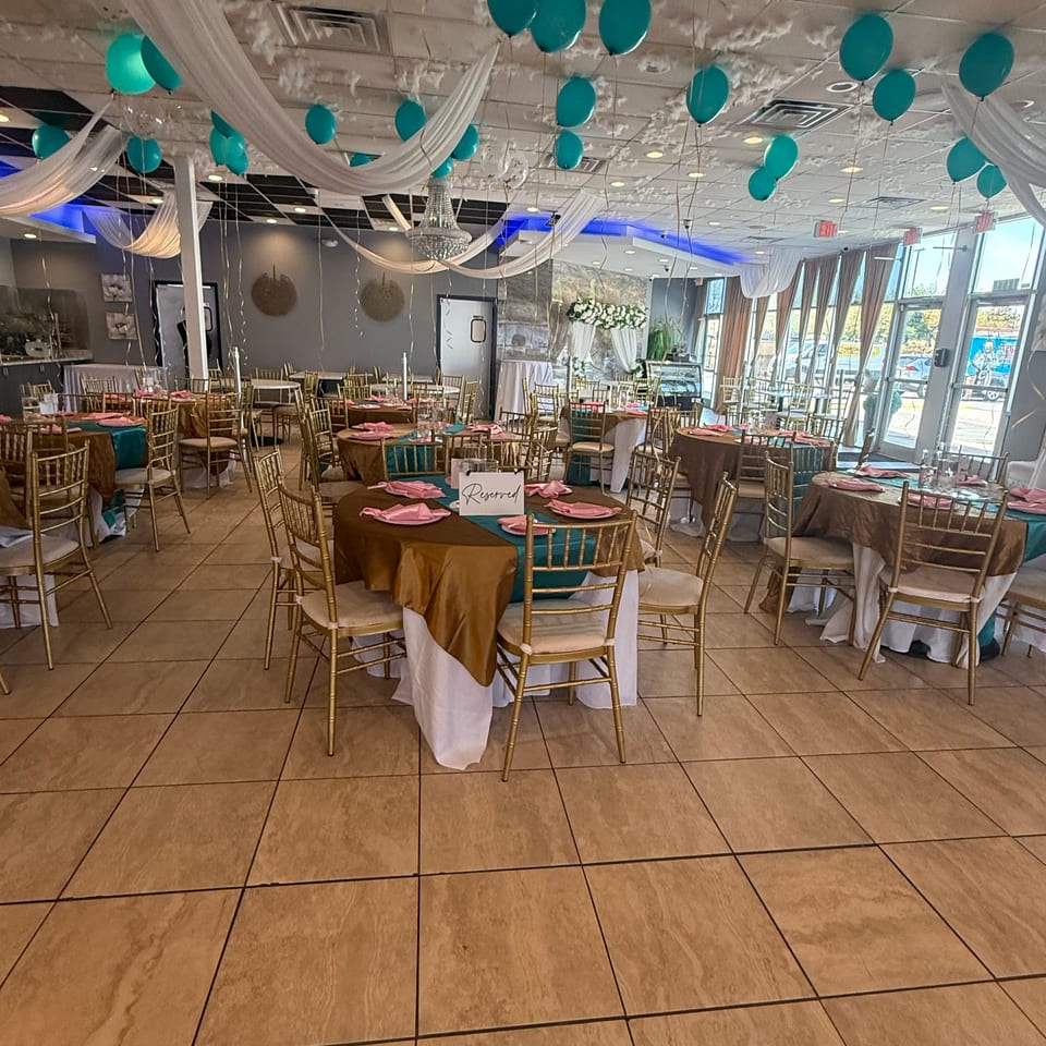 Restaurant dining room decorated with teal and gold tables, pink napkins, and teal balloons on the ceiling.