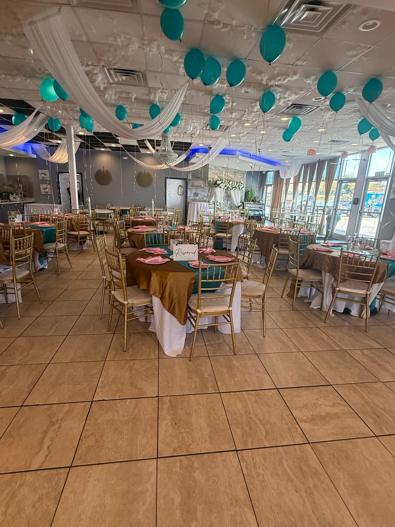 Restaurant dining room decorated with teal and gold tables, pink napkins, and teal balloons on the ceiling.