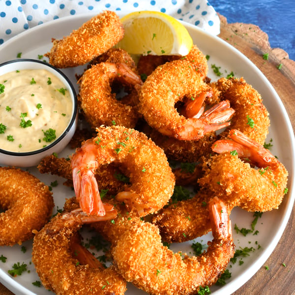 Crispy breaded shrimp with a side of creamy dipping sauce, garnished with parsley and a lemon wedge.