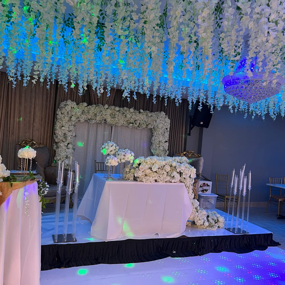 Elegant event space with white floral decor, a cake, and a light-up dance floor.