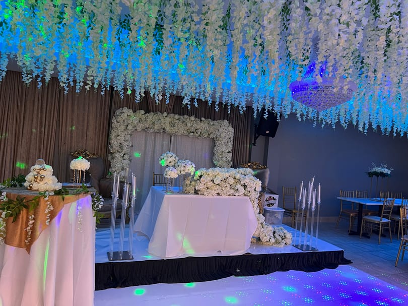 Elegant event space with white floral decor, a cake, and a light-up dance floor.
